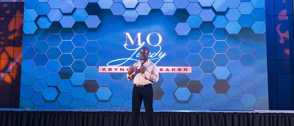 Morace wearing business attire, on stage as the keynote speaker